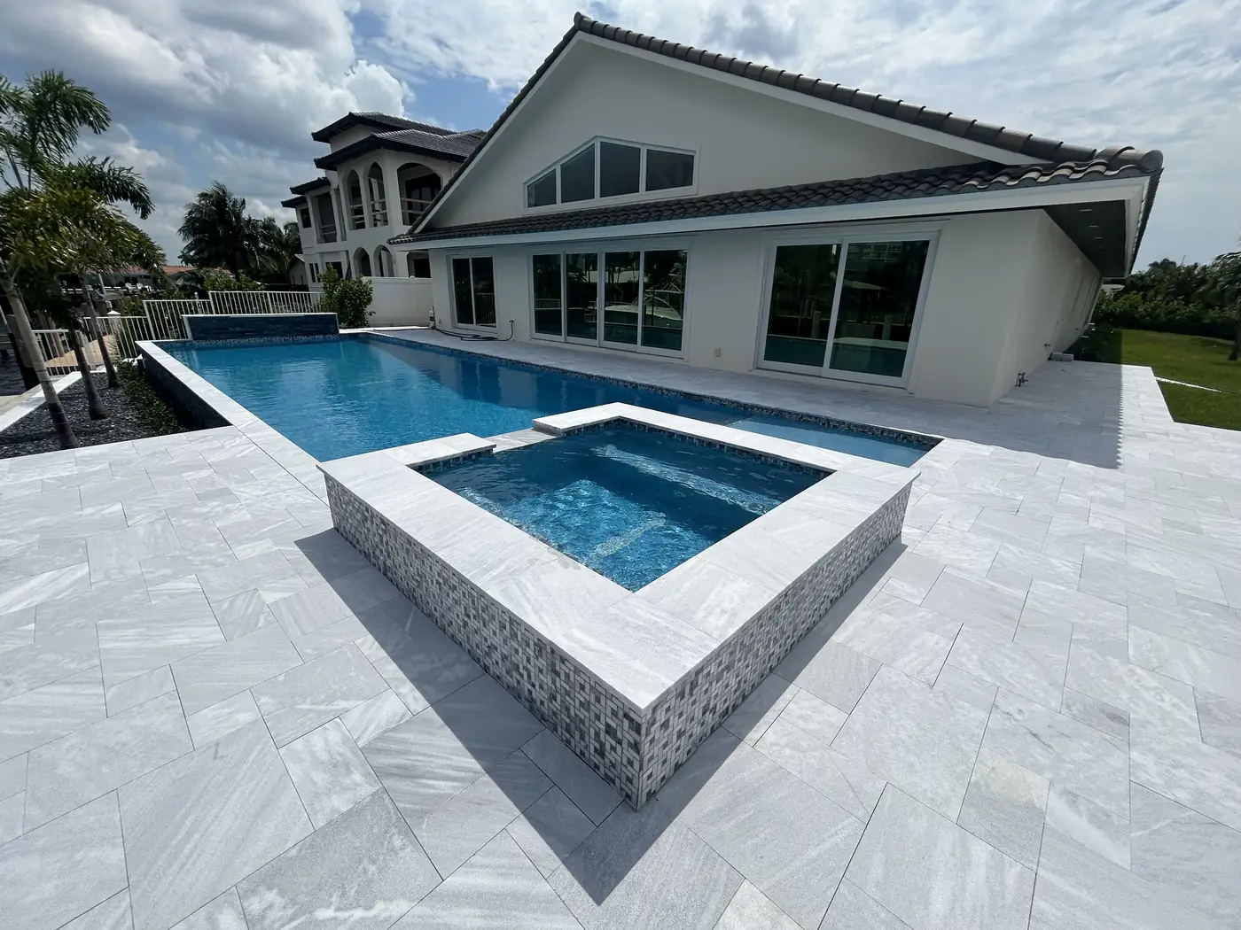 Residential swimming pool with raised spa, pale stone deck, and palm landscaping